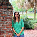 Kristin is pictured wearing a green shirt and denim pants. She is smiling.