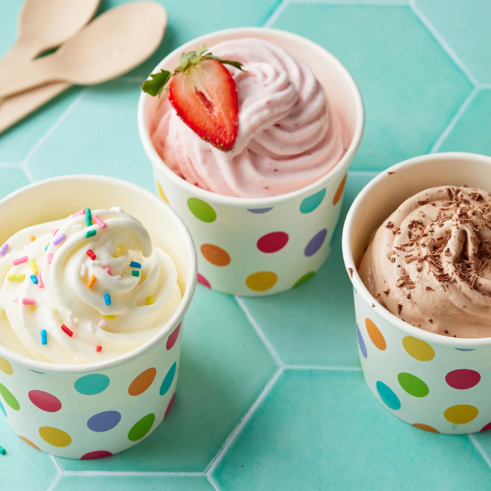 Three cups of frozen yogurt in vanilla, strawberry and chocolate flavors, topped with sprinkles, a strawberry and chocolate shavings.