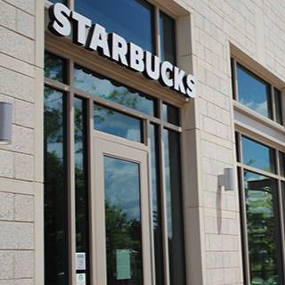 Exterior entrance of a Starbucks location with the Starbucks sign above glass doors and windows.
