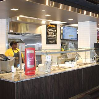 QDOBA food service counter with a glass serving station, digital menu board and employee behind the counter.