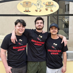 Three Breakfast Jawn staff members wearing matching black T-shirts stand together outside beneath a breakfast-themed sign.