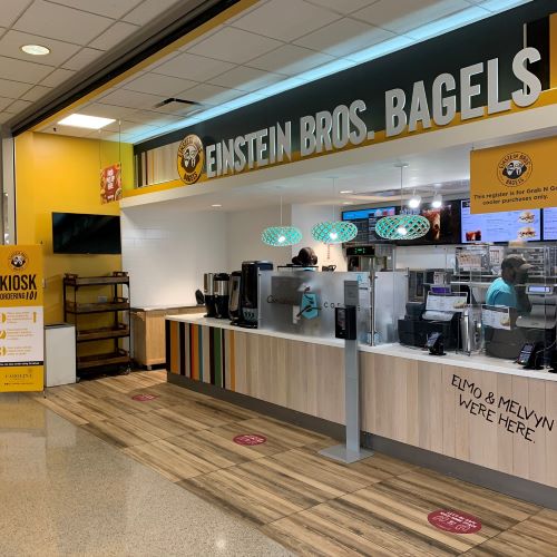 Einstein Bros. Bagels counter with ordering registers, menu screens, coffee equipment, and staff behind the counter.