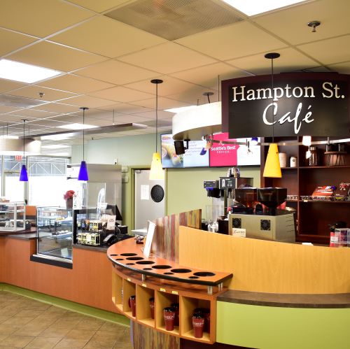 Hampton St. Café counter with coffee machines, display cases, colorful pendant lights, and a curved wood service counter.