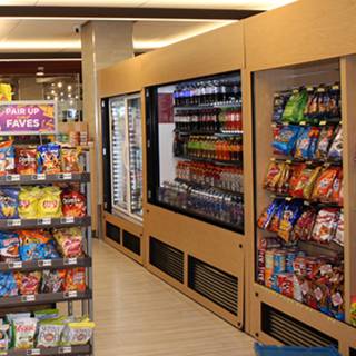 Convenience store aisle with refrigerated beverage cases and shelves stocked with chips, candy and other snacks.