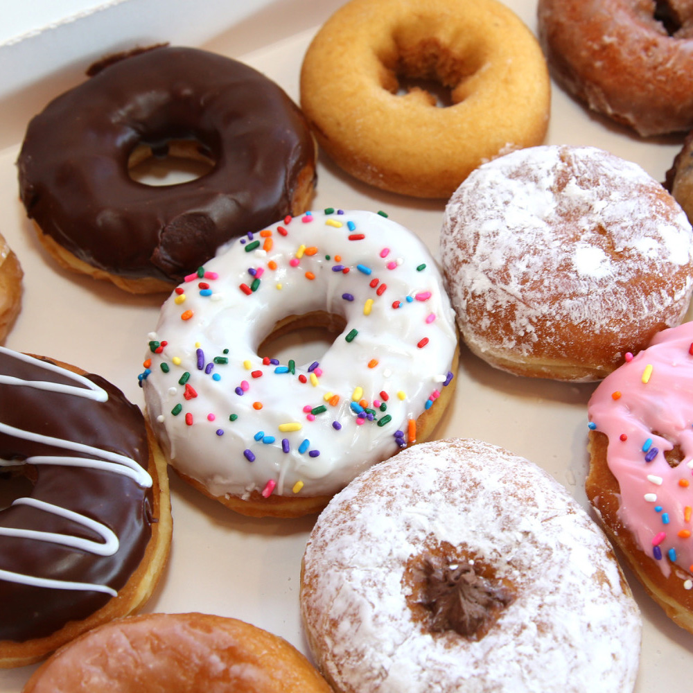 Assorted donuts with chocolate, vanilla and pink icing, colorful sprinkles, powdered sugar and glazed toppings.