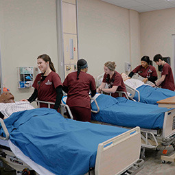 Female nursing student in red scrubs doing a bed check on a patient