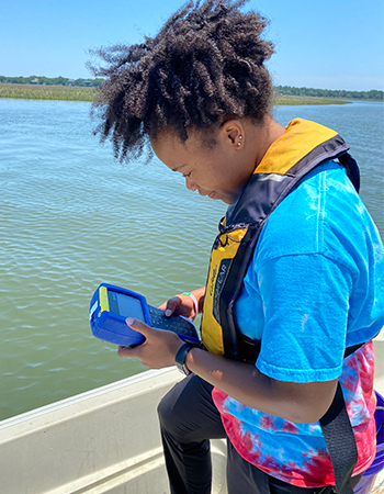 Researcher holding a water meter on a boat on the coast.