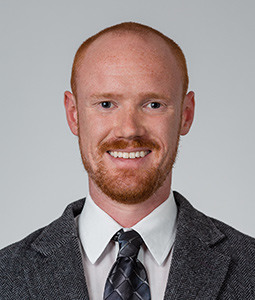 a man with a gray suit on smiling in front a light gray backdrop
