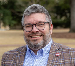 a photo of a man outside with a plaid jacket on smiling 