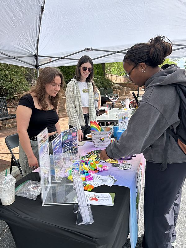 Students staff a Harriet Hancock Center outreach table under a white tent as a visitor looks through displayed materials.