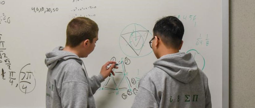 Two boys doing math on a whiteboard.
