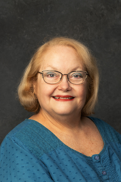 a photo of a woman with blonde hair and redish glasses on smiling indoors