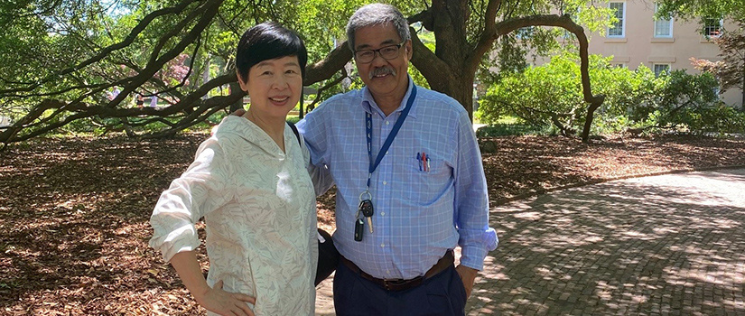 man and woman standing outside under trees smiling.