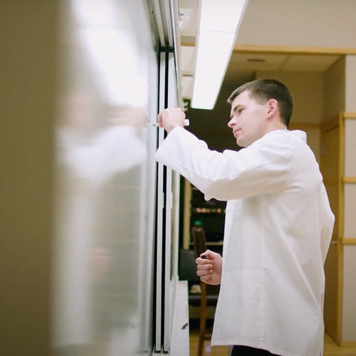 Man in white coat writing on a white board