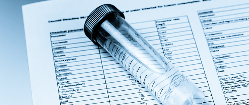 Clear sample vial filled with water resting on a printed chemical analysis report listing contaminants and measurement values.