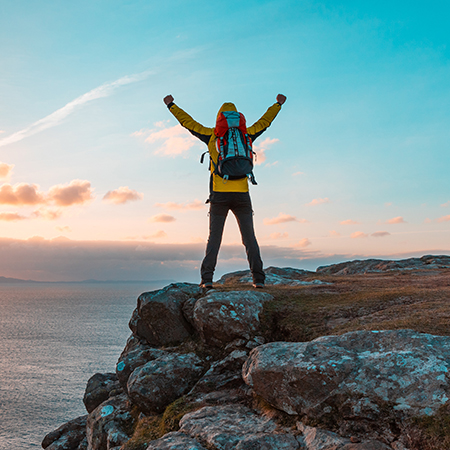 Happy successful man with arms up on the top of cliff in Scotland at sunset