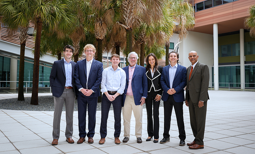 John Harloe with former Dean Rohit Verma and the 2023-24 recipients of the S. Travis Pritchett Investments Scholarship; group is standing in the Moore School Courtyard with palmetto trees in the background