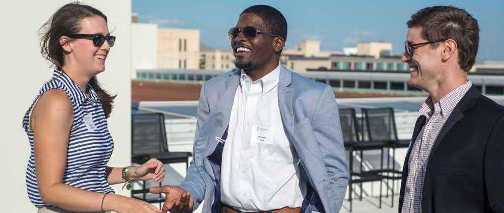 Three members of the Moore School alumni community attending a networking event on the rooftop of the Moore School