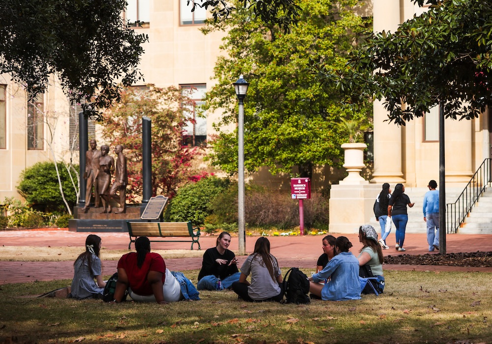 group of students sitting in a circle on the ground in front of a statue