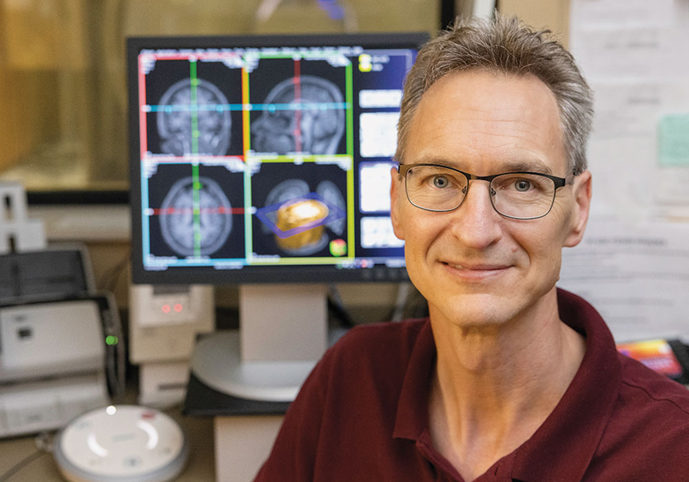 Chris Rorden smiles for the camera with the MRI machine in the background.