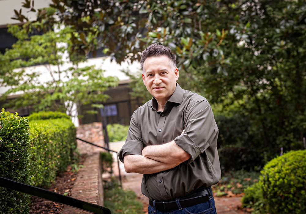 Brett crosses his arms in a green space on campus
