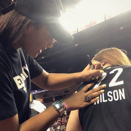 A woman signs an autograph with someone's aid