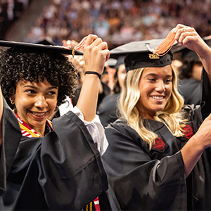Two women in caps and gowns turning tassles on graduation caps
