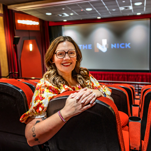 Woman sits in a movie theater with the words 'The Nick' projected on the screen in the background.