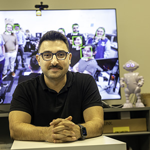 Assistant professor Ramtin Zand poses in the iCAS lab with ABii the social robot.