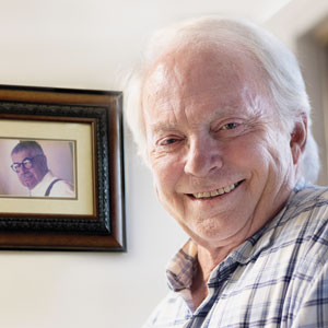 Rick Layman smiles for the camera with Matt Bruccoli’s photo in the background