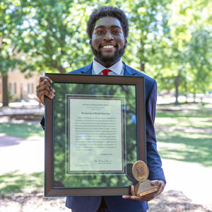 man stands outside holding a framed award