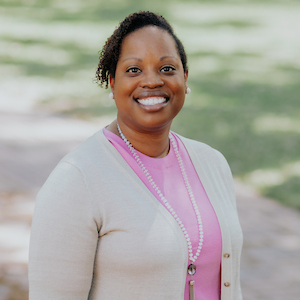 woman in pink shirt and white cardigan smiles at the camera