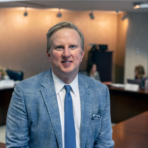 Man stands in front of a conference table with people in the background