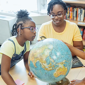 A teacher and two students identify a location on a desktop globe.