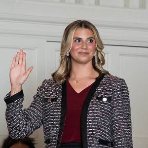 woman stands with her right hand raised