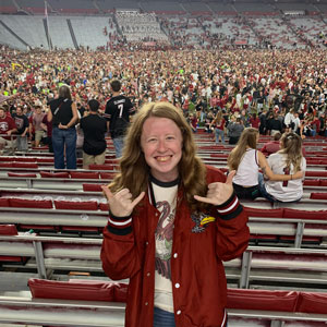 woman standing in a football stadium giving the 'spurs up' hand sign