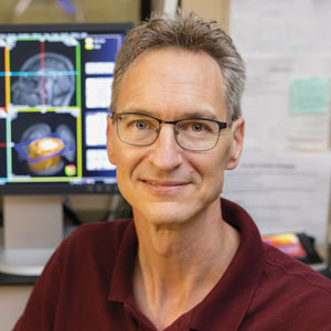 Chris Rorden smiles for the camera with the MRI machine in the background.