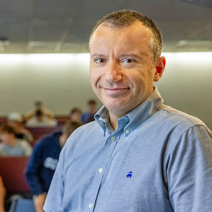 Nikos smiles in front of his class as they take their seats in a lecture hall.