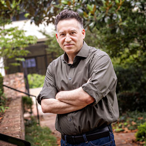 Brett crosses his arms at looks directly at the camera outside on campus