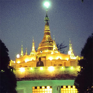 A golden pagoda building with several steeples is lit against evening sky