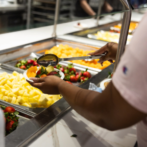 A person holding a plate and putting food on the plate from a food hall.